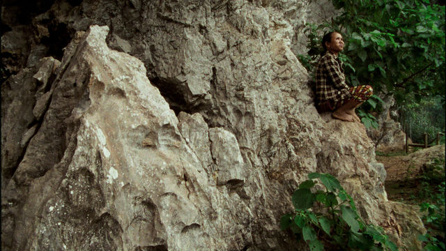A man perches on a large, craggy rock