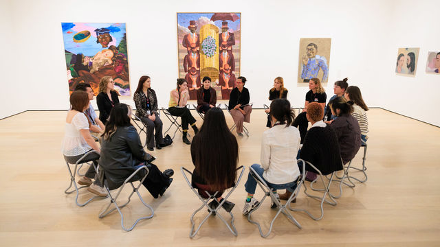 A group of people sit on folding chairs in an art gallery