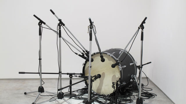 A bass drum sits on the floor surrounded by an array of microphones