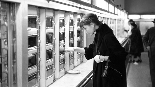 Black and white photo of Audrey Hepburn inspecting items in an automat