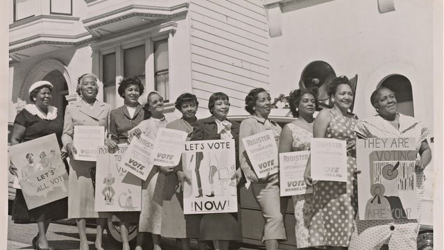 A black-and-white photograph of ten women lined up with signs along the Citizenship Education Project's motorcade route encouraging voting and voter registration.