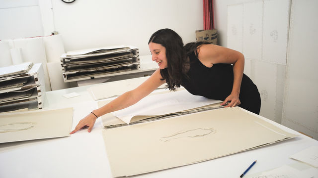 Analia Saban leans over a table to point at a print