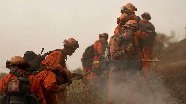 A line of inmates dressed in orange firefighting gear, digging a trench