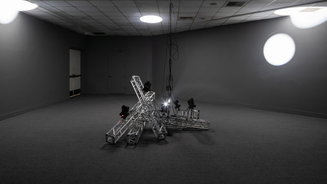 A metal installation at the center, with light and shadow in the background.