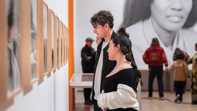 Visitors viewing a row of framed works installed on a gallery wall