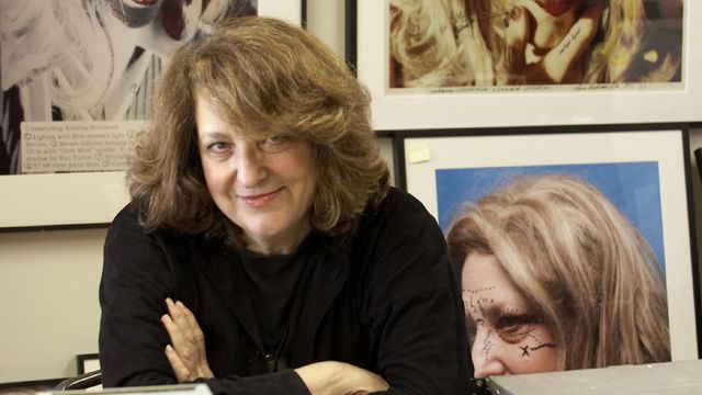 Lynn Hershman Leeson in her office with framed artwork on the walls behind her