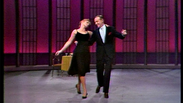 Fred Astaire dances arm-in-arm with a woman in a black dress