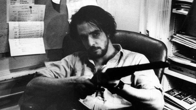 still from ice of a man sitting pointing a shotgun