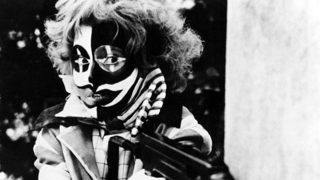still from third generation of woman wearing mask and holding gun