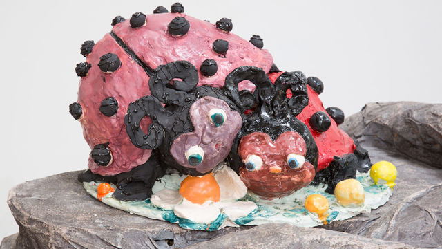 Sculpture of two ladybugs with noses and large eyes laying on top of each other