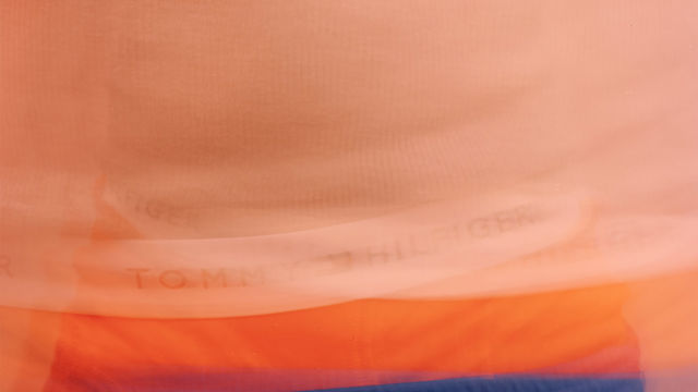 Blurred image of a torso wearing blue shorts with orange boxers peaking above the waistband, the white band of the underwear reading "TOMMY HILFIGER" in black letters
