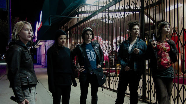 Five people stand on the sidewalk in front of a shuttered storefront