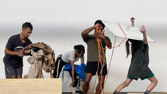 Five dancers in casual clothing interact with contsruction materials