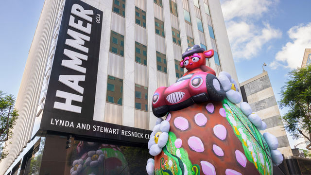 Massive outdoor inflatable portraying a stern-eyed bear in a hot-pink convertible atop a strawberry-studded shaped hilltop with daisies