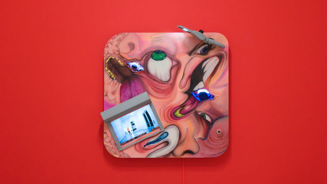 Square multi-media work with distorted images of faces and video screens, on a bright red wall