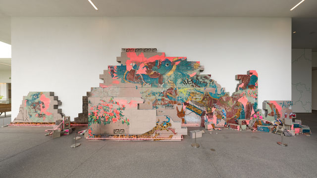 Installation featuring a crumbling wall of cinderblocks with handpainted images and pink neon lights