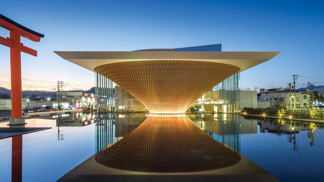 A glowing building in the shape of an inverted pyramid, with a reflecting pool in front of it