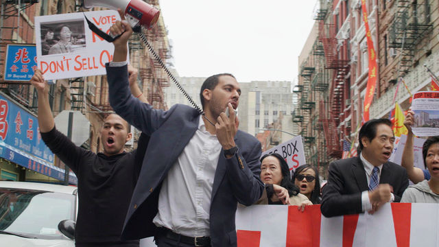 A man with a loudspeaker stands at the front of a large protest