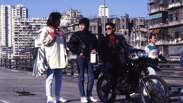 Three youths, one sitting on a motorcycle, in a city