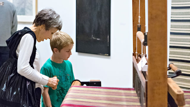 A woman and young boy look at an artwork on a loom