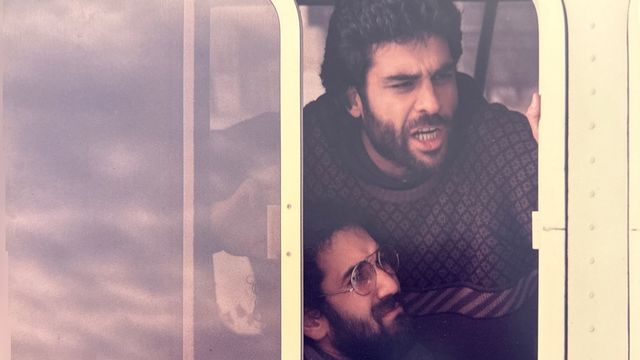 Two men lean out of an open bus window