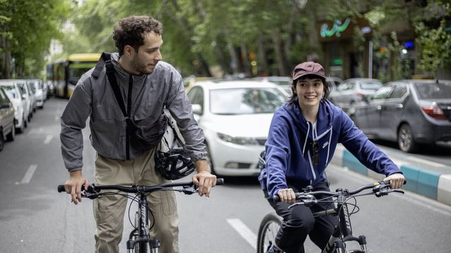 A young man and woman bike down a city street