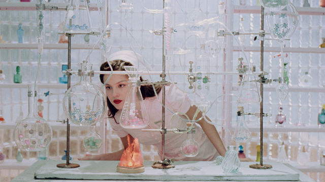 Olivia Rodrigo looks intently at a glass beaker while wearing a vintage nurse outfit