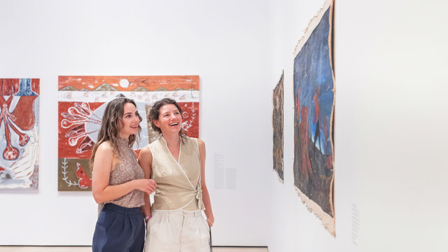 Two women look at a painting on a gallery wall together