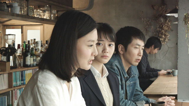 Two women and a man, viewed in profile, sit at a bar counter