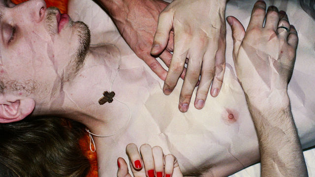 Crumpled image of a pale, topless man laying prone with two hands placed on their chest