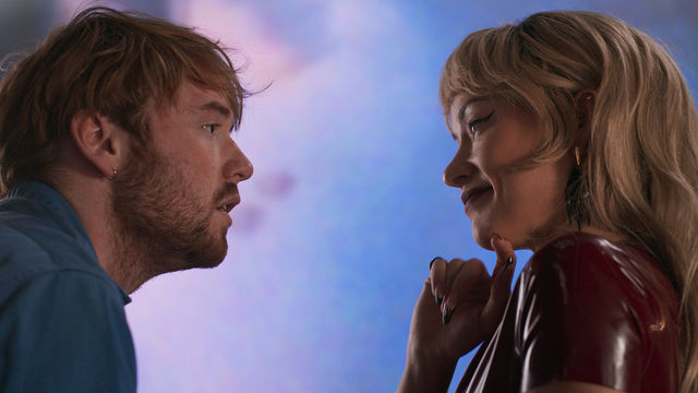 On the left, a man with short, scruffy blond hair and beard gazes into the eyes of a woman with wavy, blond hair
