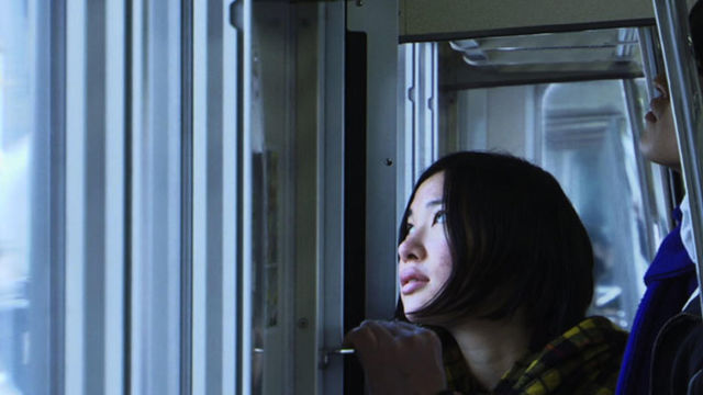 A woman with a short, dark bob haircut looks out of a window