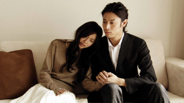 A mand and woman sit on a couch holding hands
