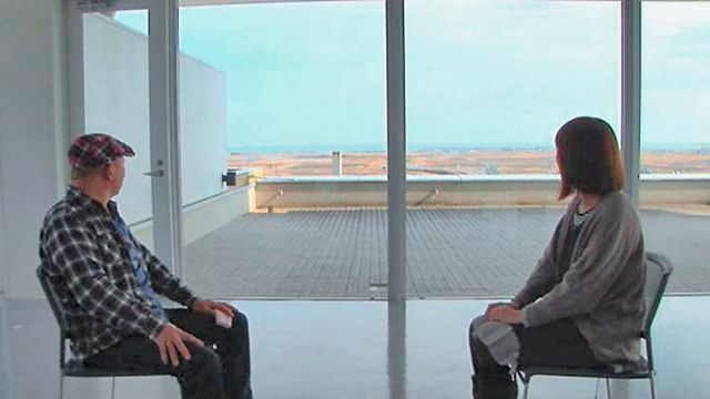 A man and woman sit across from each other, looking out a window