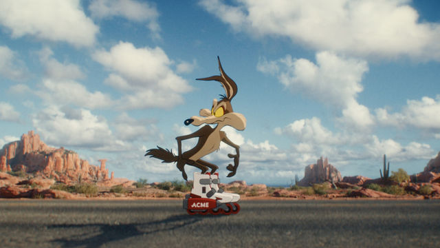 A cartoon coyote wearing ACME brand rollerblades stands on an empty desert highway