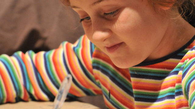 A young girl smiles while writing on brown paper