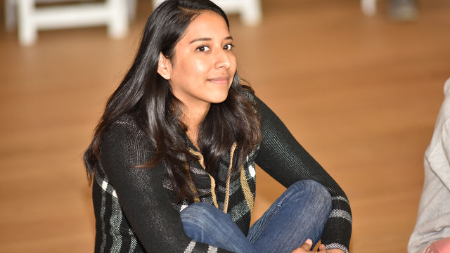 Russel Altamirano smiles at the camera, siting cross-legged and  on the hardwood floor at the Hammer Museum