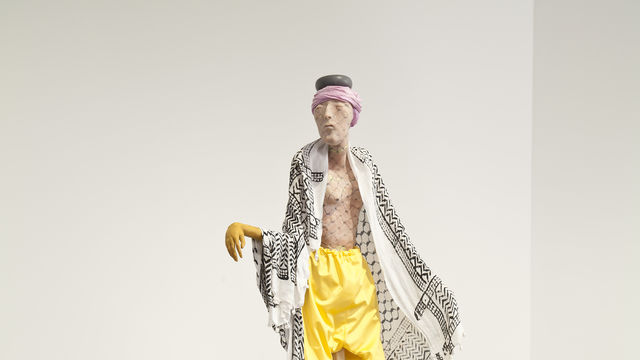 A sculpture of a man dressed in yellow pants stands on a black plinth