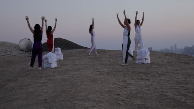 Five figures stand with their arms up, walking across a hill