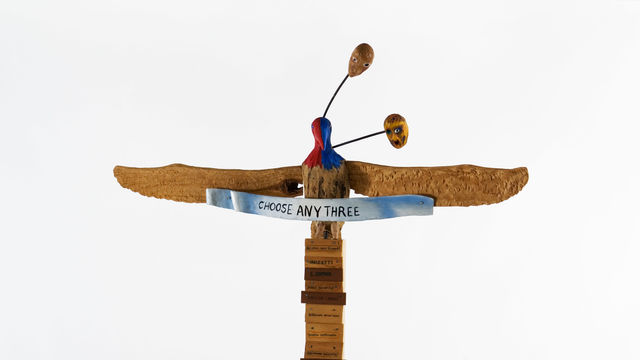 Tall wooden sculpture topped by a bird with outstretched wings