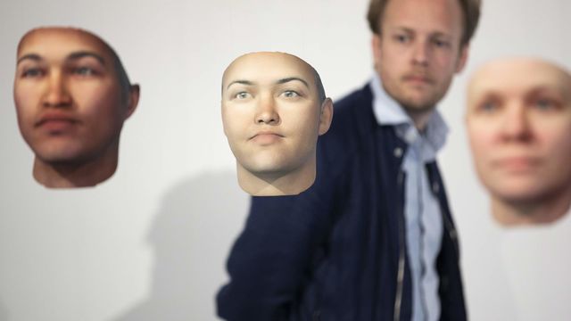 Floating computer-generated human faces are viewed by blurred out person standing in the background.