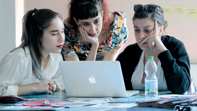 Three women look over a laptop together