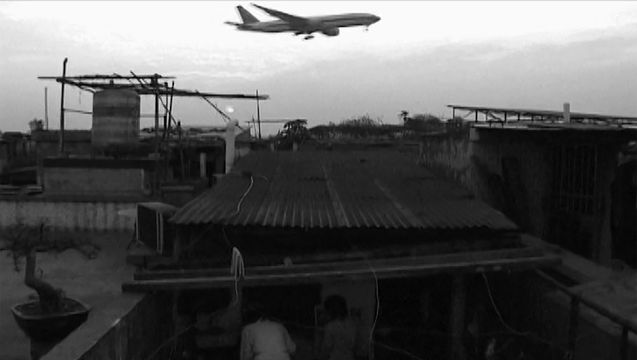 Black and white image of an airplane flying over a village