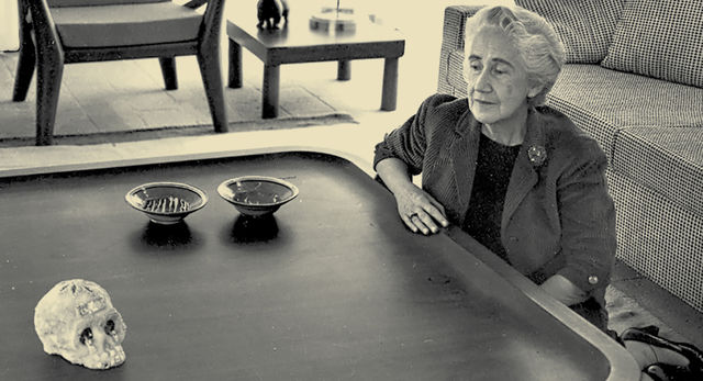 Clara Porset sits on the floor next to a large wooden coffee table