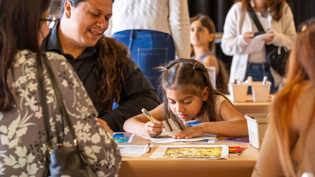 Child draws at a table while adults look on