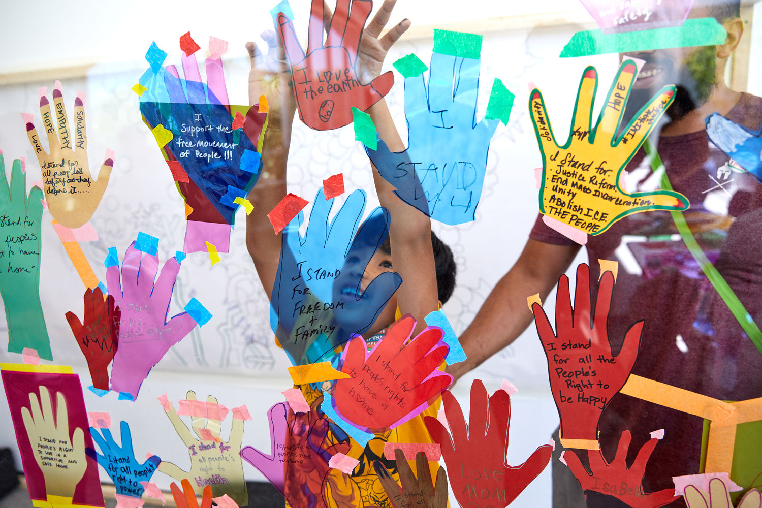 A child presses his hands to a glass covered in paper hand cut-outs