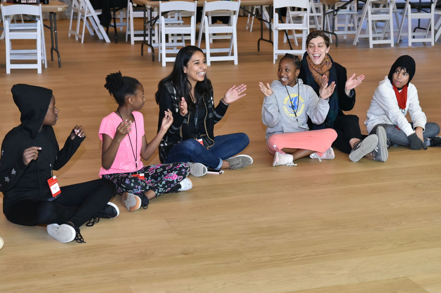 A line of children and teachers sitting on the floor, clapping