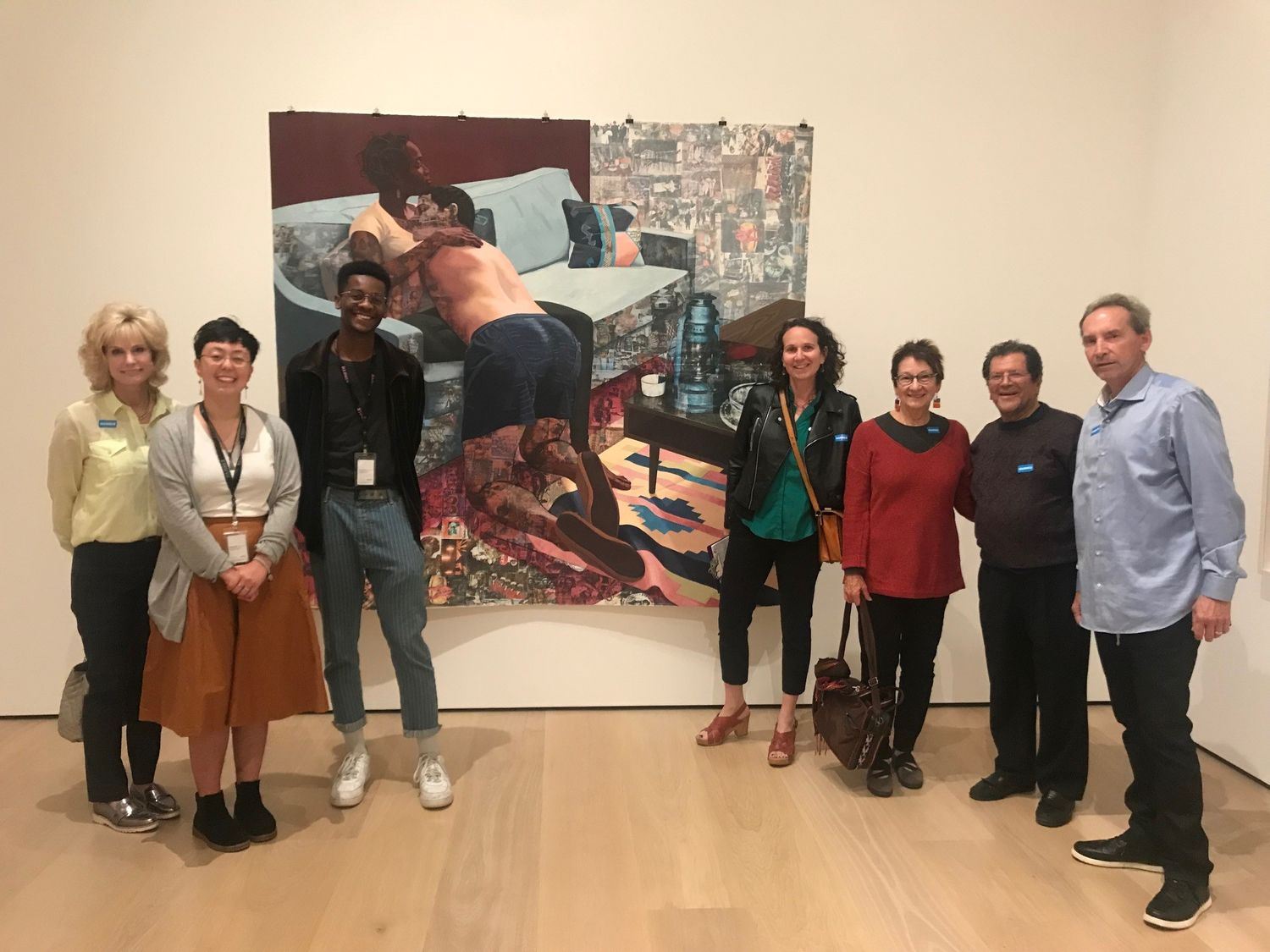 A group of people stand before a painting in a gallery and smile at the camera