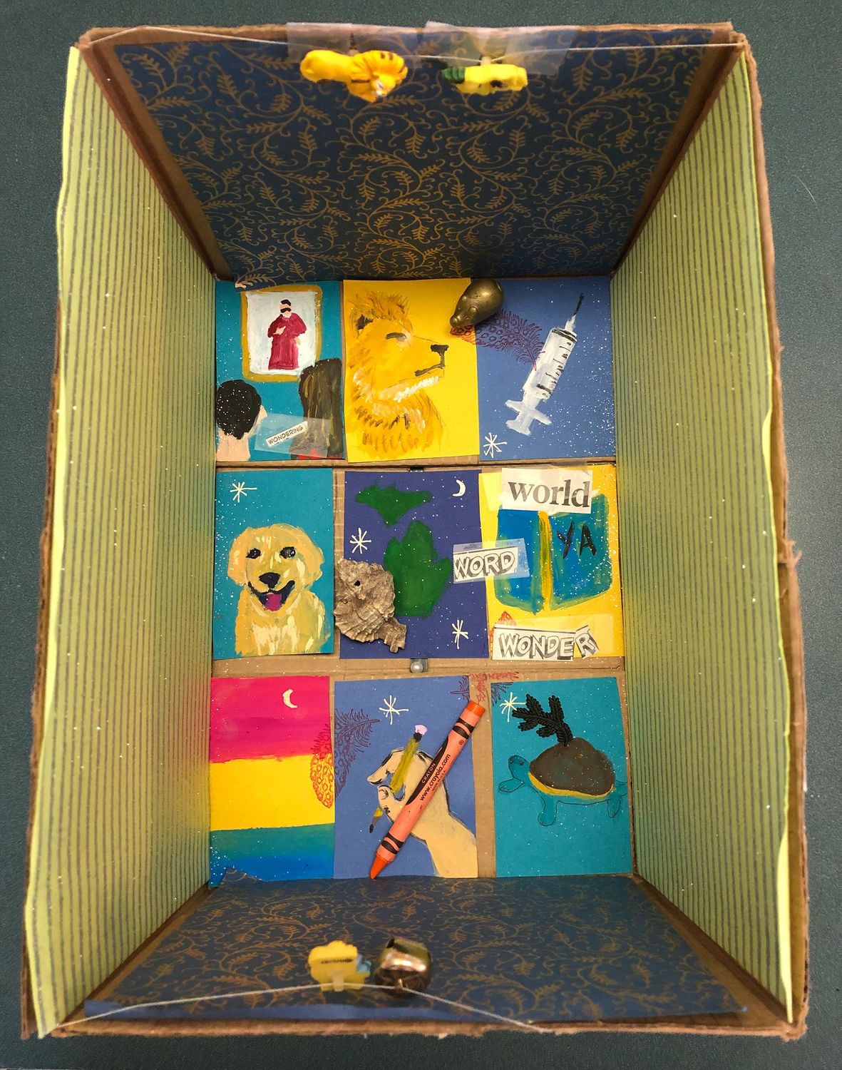 Photo looking down into a box that has been decorated with small painted images on cardboard. 