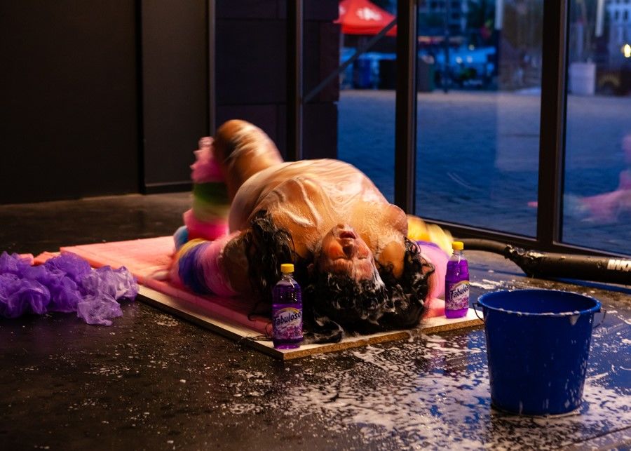 A woman reclines on the floor and covers herself with cleaning agents